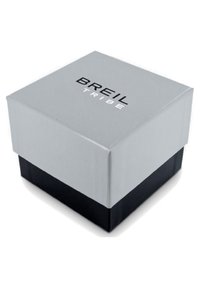 Boîte d'emballage carrée en gris et noir, avec une texture lisse. Le dessus présente le texte "BREIL TRIBE" en lettres noires en gras.