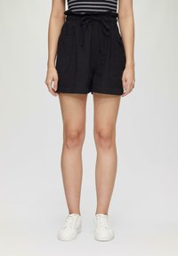 Shorts en lin noirs avec un waist à cordon, deux poches avant et une coupe décontractée. Associés à des baskets blanches, soulignant un look décontracté.