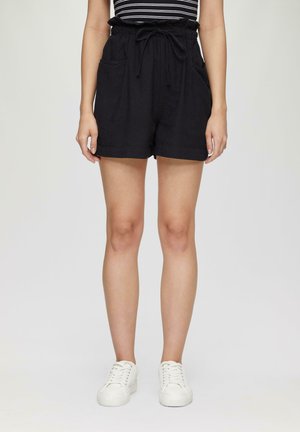 Black linen shorts with a drawstring waist, two front pockets, and a relaxed fit. Paired with white sneakers, emphasizing a casual look.