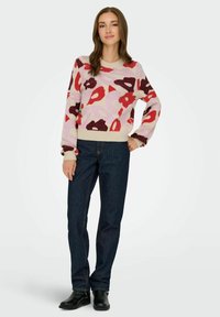 Pull en tricot avec un motif floral multicolore en rose, rouge et violet, associé à un jean bleu foncé et des bottes chelsea noires.