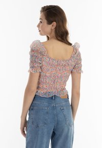 Top trasparente con motivo floreale, maniche a sbuffo corte, orlo arricciato e scollatura quadrata sulla schiena, abbinato a jeans di denim a vita alta.