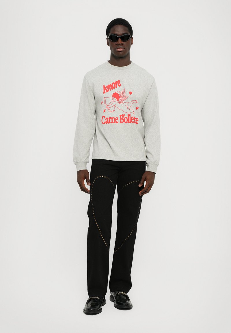 Gray sweatshirt with red graphic print and text, black pants with gold star accents and curved seams, paired with black shoes and sunglasses.
