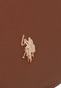 Borsa in pelle marrone con texture, dotata di un emblema dorato in rilievo che raffigura tre cavalieri. La superficie presenta una delicata finitura a motivo.