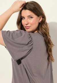 Camiseta gris con mangas abullonadas, material de algodón suave, delicada costura blanca a lo largo de los bordes de las mangas, corte casual.