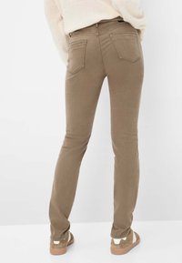 Jeans skinny marroni con una texture liscia, design a cinque tasche e cuciture in contrasto. Abbinati a calzature marroni chiare con accenti bianchi.
