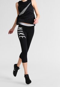 Top atletico nero senza maniche con un accento riflettente e leggings neri aderenti alla caviglia con la scritta bianca "NIKE". Scarpe da corsa nere.