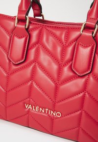 Röd quiltad läderhandväska med chevronmönster, som har guldaccessoarer och "Valentino"-logotypen i metallbokstäver på framsidan.