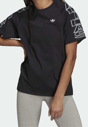 Person wearing a black Adidas t-shirt with logo on chest and large Adidas text on sleeves, paired with light gray leggings.