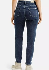 Ciemnoniebieskie rurki z wysokim stanem, z dwoma tylniymi kieszeniami i subtelnym przeszyciem. Materiał to elastyczny dżins.