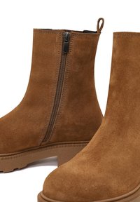 Botas de tobillo de ante marrón con cremallera lateral, suela texturizada y tirador en la parte trasera para una fácil puesta.
