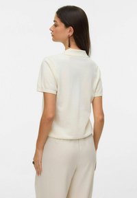 Krótkorękawowa dzianinowa koszulka polo w kolorze ecru o miękkiej fakturze, z kołnierzykiem i luźnym krojem, w połączeniu z beżowymi spodniami.