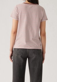 Striped t-shirt in light pink and mauve, short sleeves, soft fabric, classic fit. Paired with high-waisted dark gray jeans, textured cotton.
