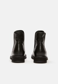 Bottines en cuir noir avec une finition lisse, des panneaux latéraux élastiques et un talon empilé. Pas de marquage visible à l'arrière.