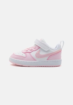 Hvid og lyserød småbørns sneakers med velcrorem, snørebånd og Nike swoosh-logo på en ensartet lysegrå baggrund.