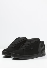 Schwarze Sneaker mit einem Obermaterial aus Wildleder, Schnürung auf der Vorderseite, strukturierten seitlichen Akzenten und einer Gummisohle; mit dem "etnies"-Logo in Schwarz.
