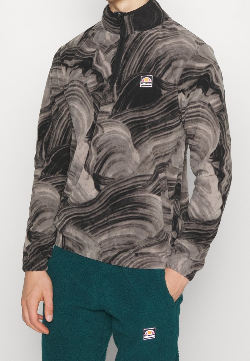 Zwart- en grijs gemarmerde fleece pullover met een half-rits kraag en logo op de bovenste linkerkant. Zachte textuur; lange mouwen. Gecombineerd met teal gekleurde broek.