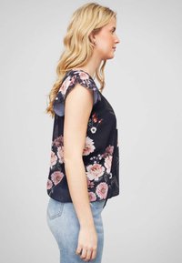 Blouse florale à manches courtes à volants, fond sombre, motifs de fleurs roses et blanches, tissu léger, coupe ample, ourlet arrondi.