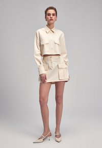 Geel gemaaid overhemd met knoopsluiting en twee borstzakken, gecombineerd met bijpassende hoge taille shorts met twee voorzakken.