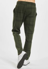 Mørkegrønne joggebukser med rutete mønster, med sidelommer og en avsmalnende design, paret med hvite sneakers.