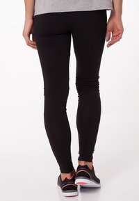 Czarne legginsy o dopasowanym kroju, wykonane z elastycznego materiału. Noszone z czarnymi trampkami z różowymi akcentami. Gładka tekstura.