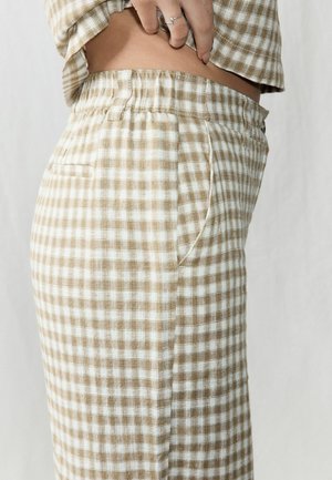 Material maro și alb în carouri, cu talie elastică și buzunare laterale, evidențiind o textură moale și o croială lejeră.