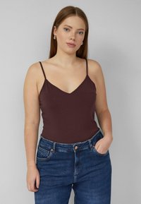 Bordeauxrode katoenen tanktop met dunne bandjes, V-hals ontwerp, gecombineerd met donkerblauwe high-waisted jeans met een voorzak.