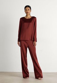 Maroonsatinarbeitsoberteil mit langen Ärmeln und weit geschnittenen Hosen. Glatte Textur, lässige Passform, minimalistisches Design mit subtiler Shine und ohne Muster.