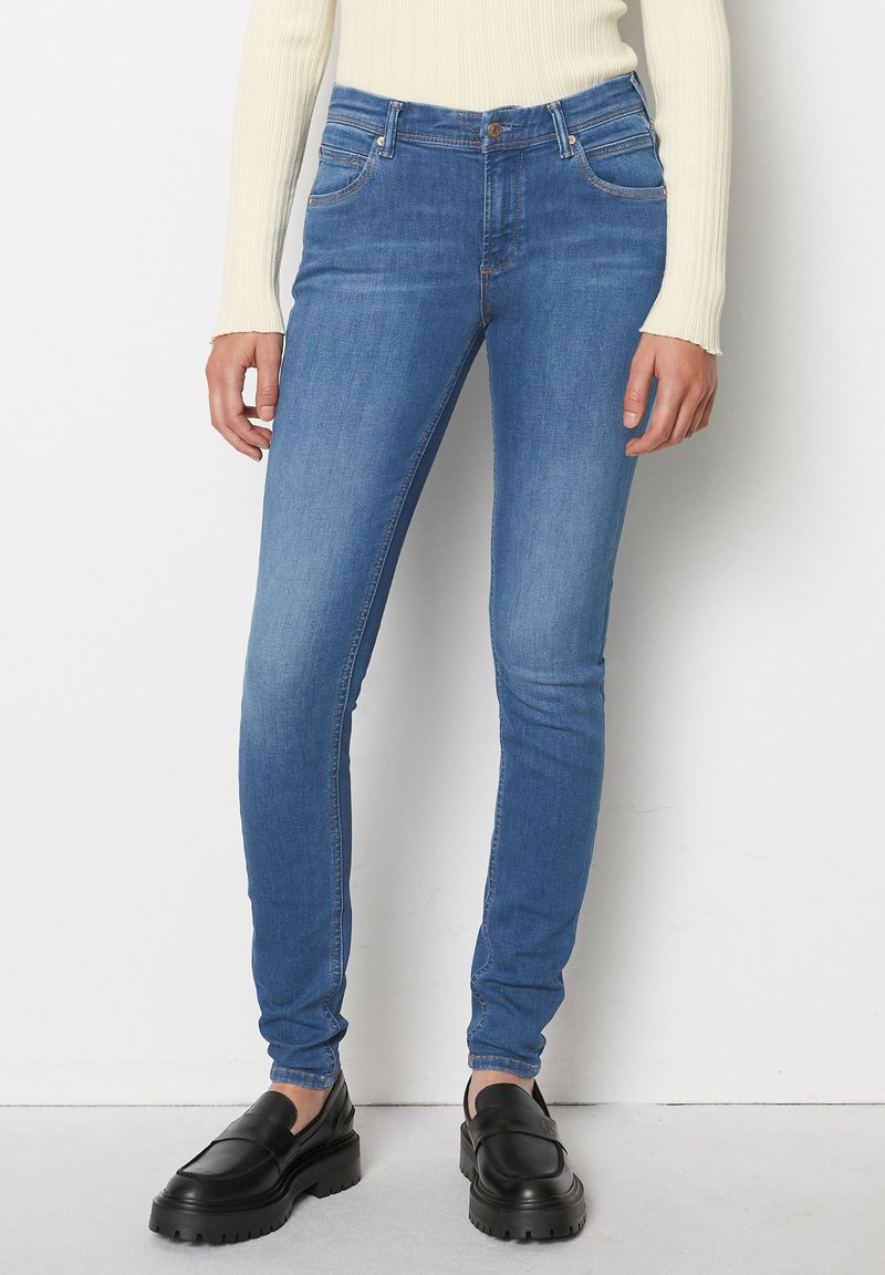 Jeans subțiri din denim albastru, cu o ușoară decolorare, patru buzunare, închidere cu nasture și fermoar, asortate cu mocasini negri cu platformă.