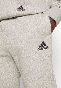 Pantalones de chándal grises de algodón con un logo negro de Adidas en la parte superior de la pierna, con cintura elástica y tejido suave y texturizado.