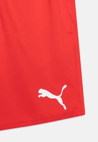 Crvene atletske kratke hlače od glatke tkanine, s bijelim Puma logotipom. Dizajn uključuje uredne šavove i standardnu veličinu.