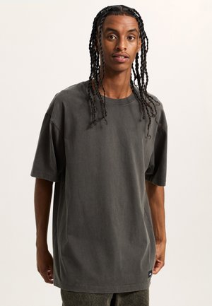 Dark grey cotton t-shirt with oversized fit, short sleeves, and a crew neck. Minimal design with a small brand label at the hem.