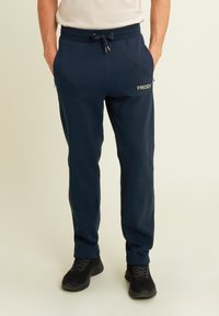Pantalones de chándal azul marino hechos de tejido suave, con una cinturilla elástica con cordón, bolsillos laterales y un pequeño logo blanco en la pierna.