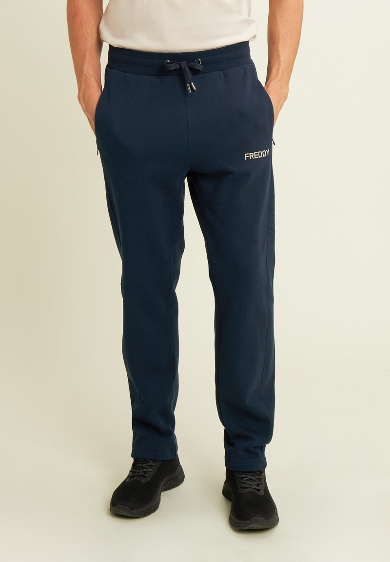 Pantalones de chándal azul marino hechos de tejido suave, con una cinturilla elástica con cordón, bolsillos laterales y un pequeño logo blanco en la pierna.