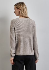 Beige gerippter Strickpullover mit langen Ärmeln, rundem Ausschnitt und lockerer Passform. Dezente Textur und weiches Material sorgen für zusätzlichen Komfort.