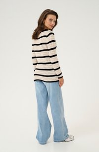 Sweter dzianinowy z czarno-kremowymi poziomymi paskami, w zestawieniu z jasnoniebieskimi spodniami typu wide-leg, o fakturowanym materiale i długich rękawach.