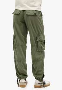 Pantalons cargo vert olive avec plusieurs poches latérales, poignets élastiqués aux chevilles et coupe décontractée, fabriqués en coton léger.