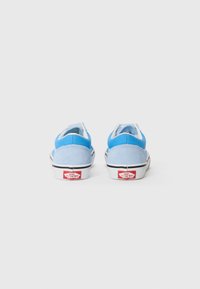 Zapatillas de ante azul con acentos blancos, cuello acolchado y suela negra. Muestra un logo rojo en el talón y un diseño aerodinámico.