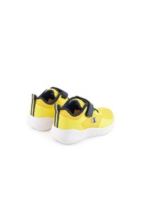 Zapatillas deportivas amarillas con parte superior de malla texturada, acentos en azul marino y suela de goma blanca. Cuenta con una correa ajustable para un ajuste seguro.