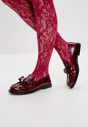 Glänzende burgunderfarbene Slipper mit einer Schleifenakzent, schwarzer Sohle, getragen mit rosa Spitzenstrumpfhosen mit floralem Muster.
