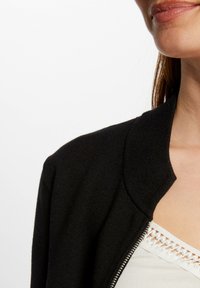 Schwarze Strickjacke mit weicher Textur, rundem Halsausschnitt und Reißverschluss. Verfügt über eine glatte Oberfläche und ein minimalistisches Design.