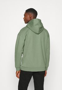 Green hoodie in soft fabric with a large hood, ribbed cuffs, and hem. The design features a relaxed fit and minimal detailing.