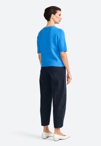 Blå kortærmet sweater lavet af letvægts, blødt materiale; parret med mørke, løse bukser og hvide slip-on sko.