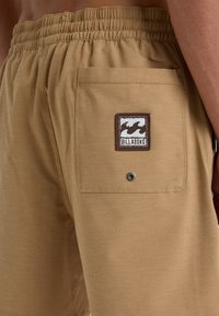Khaki plavkové šortky vyrobené z ľahkej tkaniny, s elastickým pásom a zadnou nášivkou s logom a detailom na zacvakávanie.