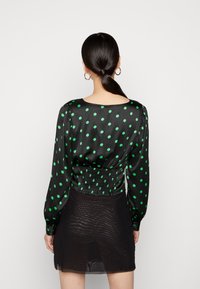 Blusa nera in satin con pois verdi, maniche lunghe a sbuffo, vita arricciata e scollatura tonda. Abbinata a una gonna nera trasparente.