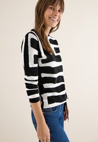 Sweter w czarno-białe paski o luźnym kroju, z długimi rękawami i sznurkiem w dolnej części. Pleciona faktura i wyrazisty wzór graficzny.