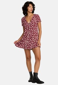 Robe florale bordeaux à manches courtes, décolleté en V, taille cintrée et détails de boutons. Associée à des bottes de combat noires.