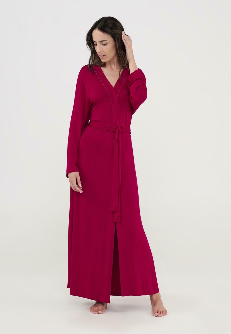 Vestido largo de manga larga en un vibrante color fucsia. Hecho de una tela suave con un lazo en la cintura y una apertura frontal. Textura lisa.