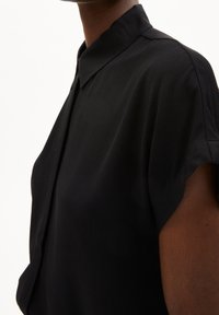 Camicia nera a maniche corte con colletto a punta, realizzata in un materiale liscio, caratterizzata da una vestibilità comoda e senza motivi o accessori visibili.