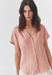 Pink linen short-sleeve shirt with a v-neck, button front, and a relaxed fit. Soft texture with a casual design, ideal for warm weather.