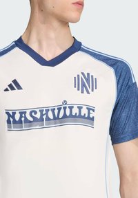 Weißes Fußballtrikot mit blauen Akzenten, mit V-Ausschnitt, kurzen Ärmeln und einer "Nashville"-Grafik in fetter Schrift, aus leichtem Material gefertigt.